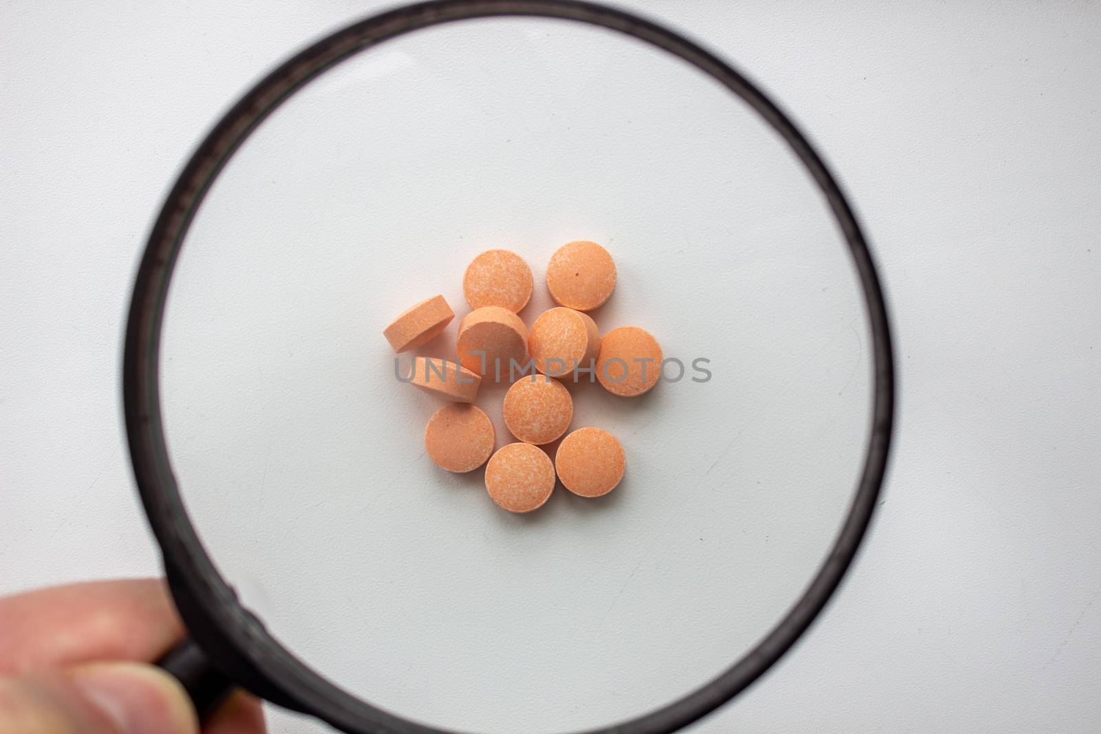 Medical tablets under a magnifying glass on a white background. by AnatoliiFoto