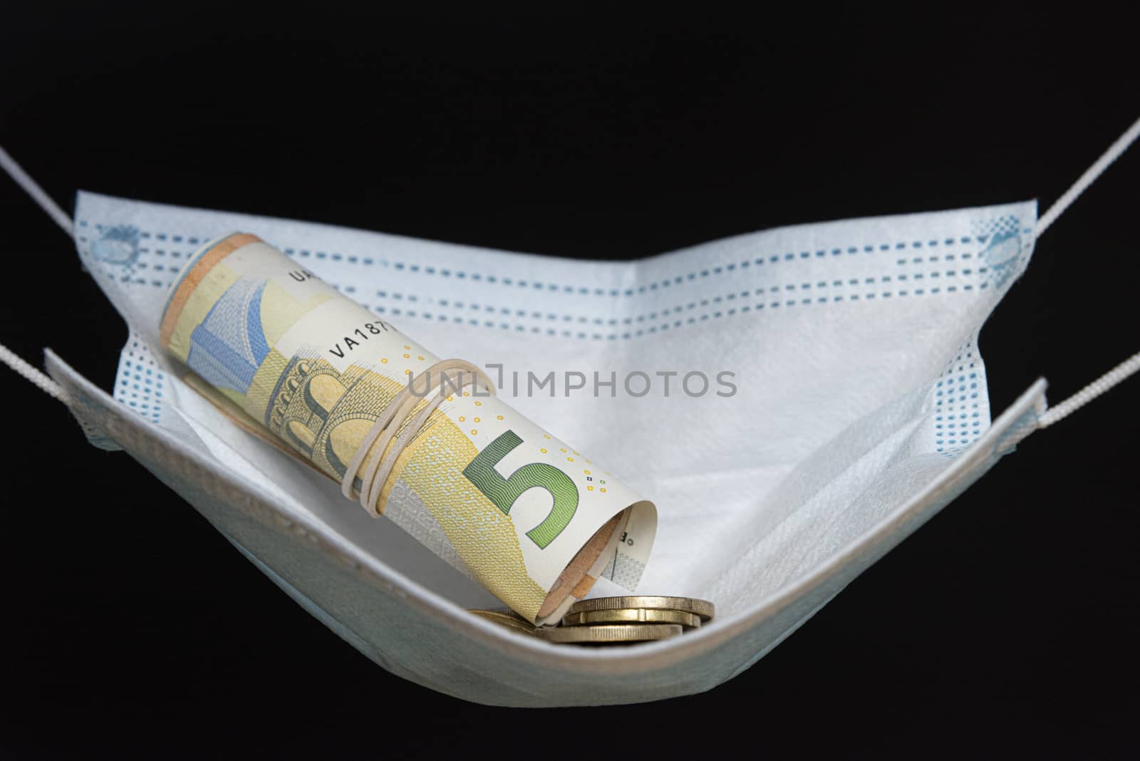 Medical face mask with money, black background. World coronavirus economic losses concept. Concept of financial impact of covid-19 on European money area. Euros and coins.