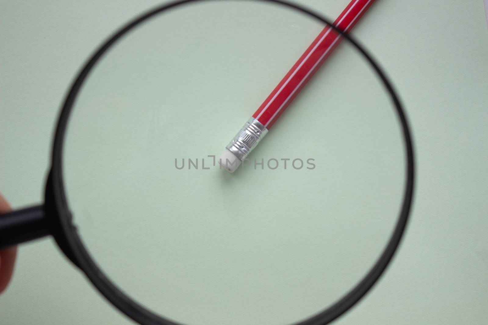 One red pencil under a magnifying glass close-up on a light background