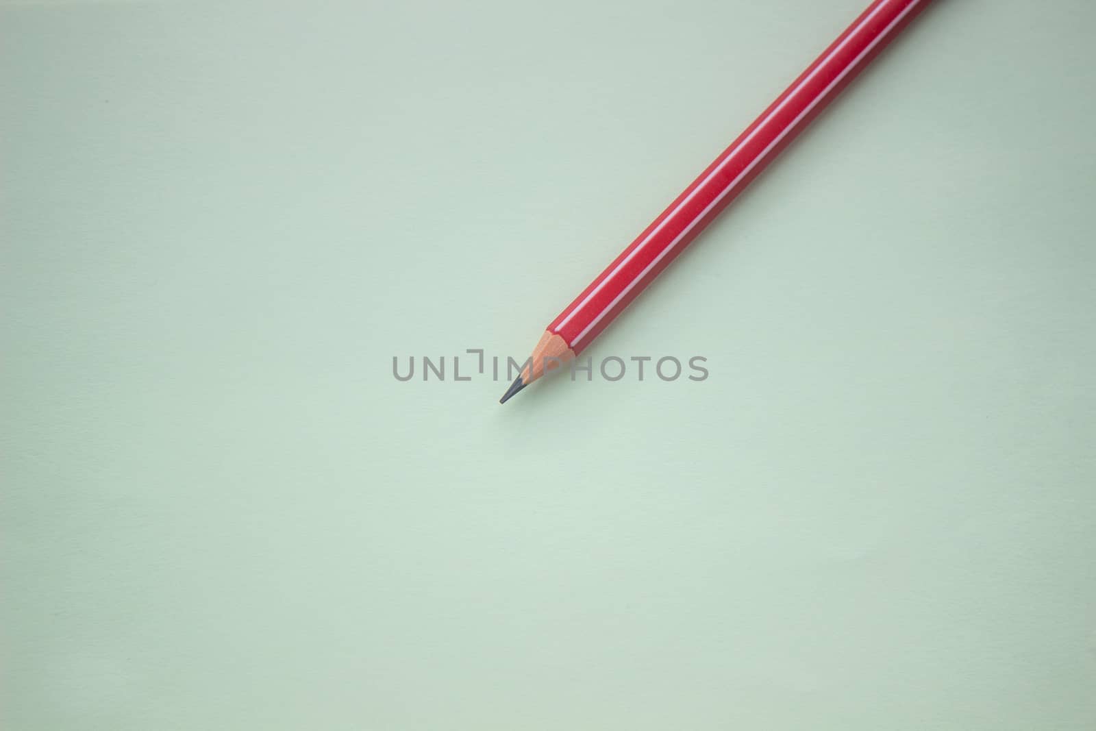 One red pencil on a light green background