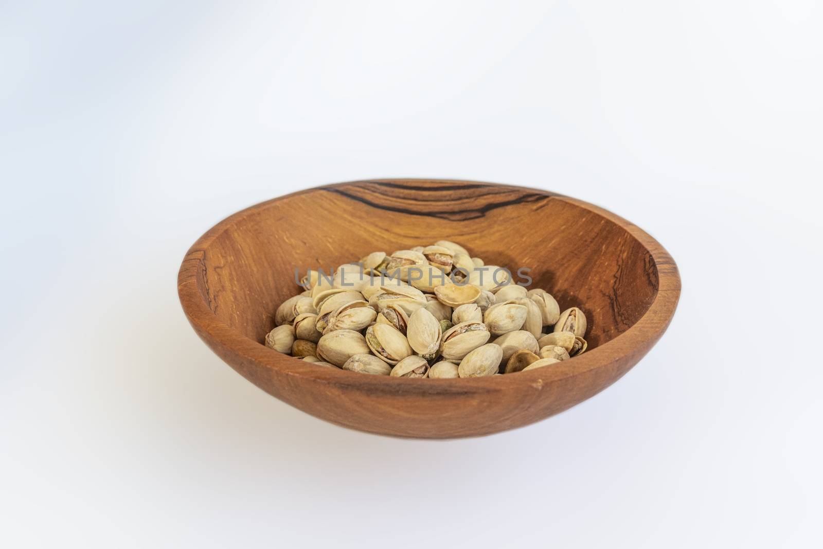 Pistachios in wooden bol as appertiser with drinks against a white background