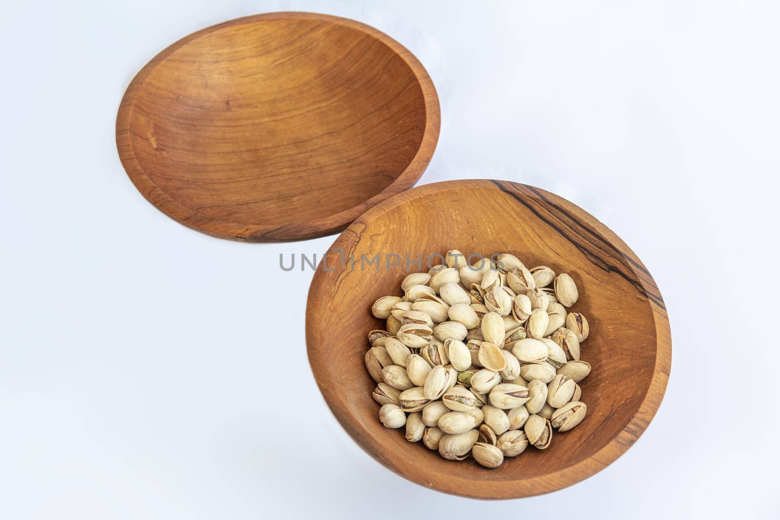 Pistachios in wooden bol as appertiser with drinks against a white background by ankorlight