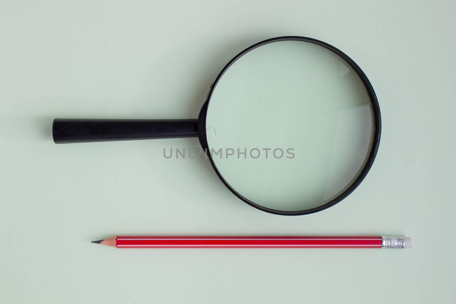 One red pencil under a magnifying glass close-up on a light background