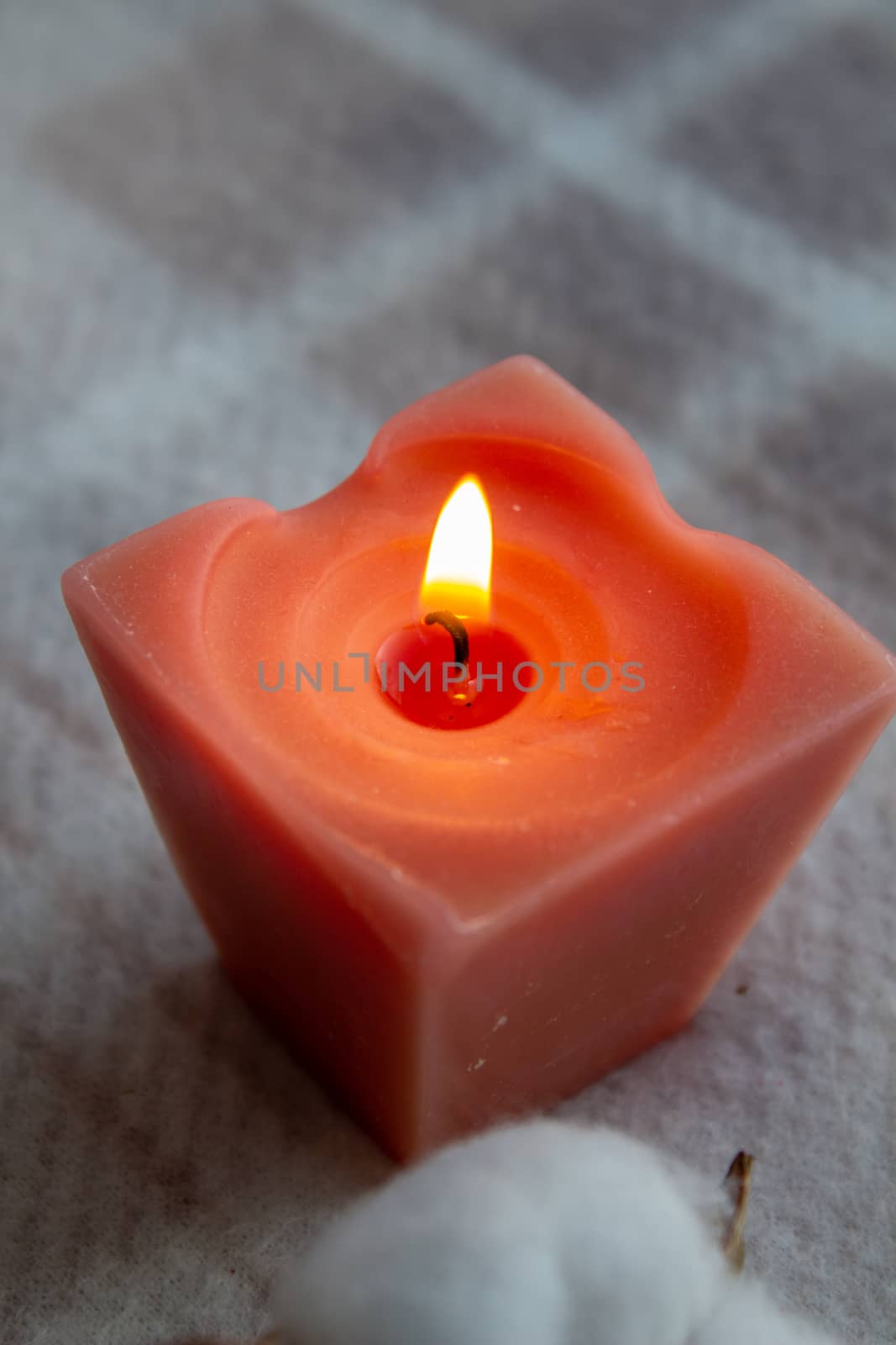 A lit red candle in the evening. The candle is on a blanket. by AnatoliiFoto