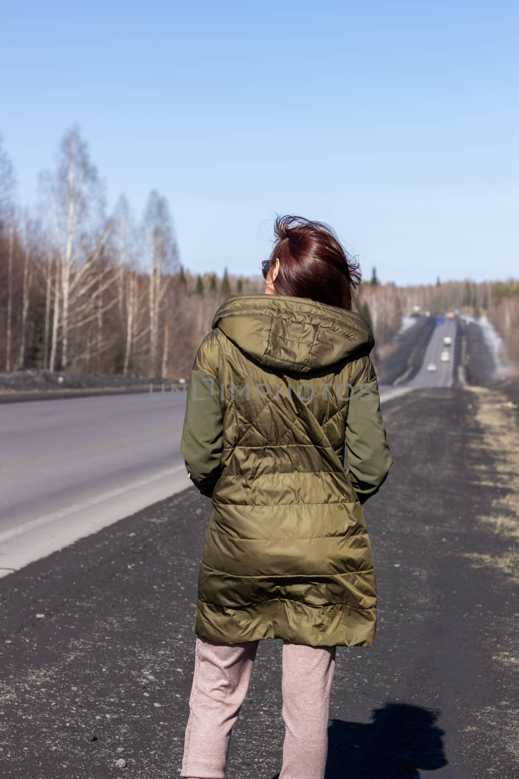 A young woman walks by the side of the road. Road in the forest.