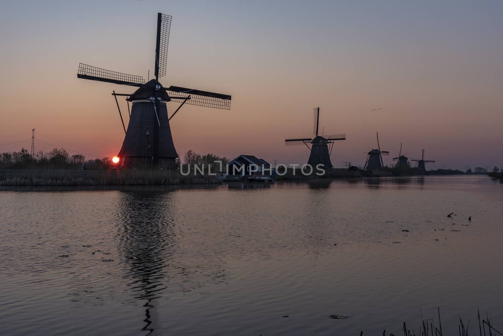 Sunrise on the alignment of windmills reflected on the calm water in the long canal  by ankorlight