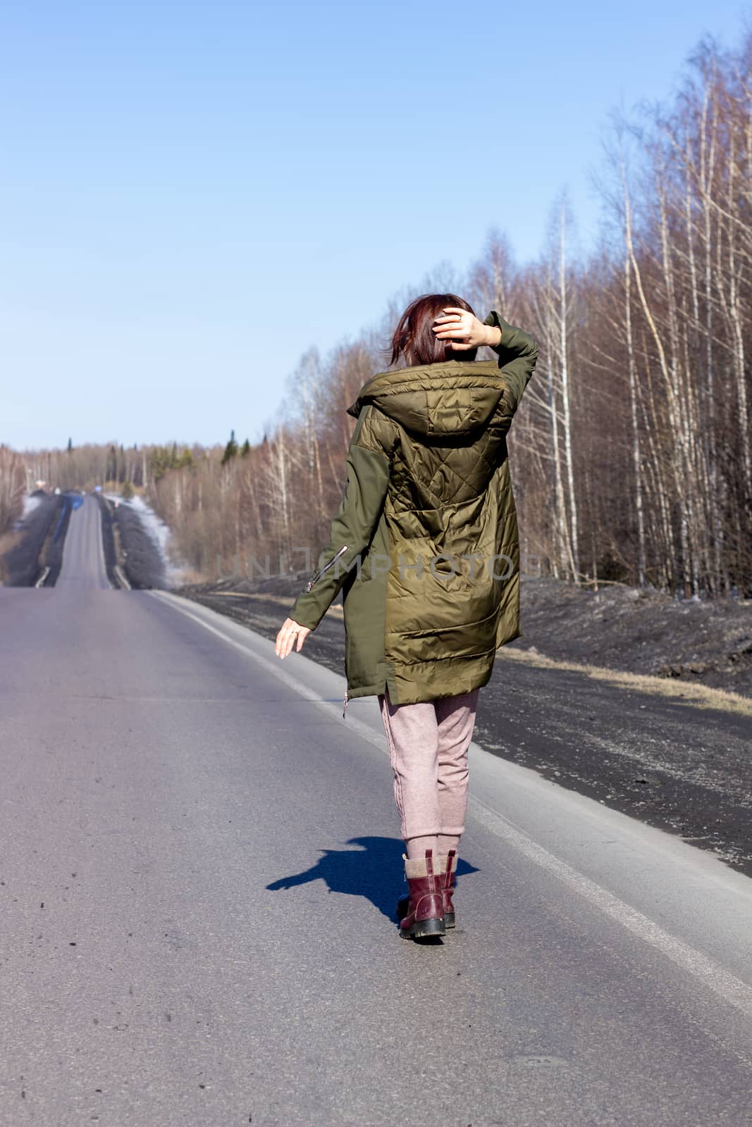 A young woman walks by the side of the road. Road in the forest by AnatoliiFoto