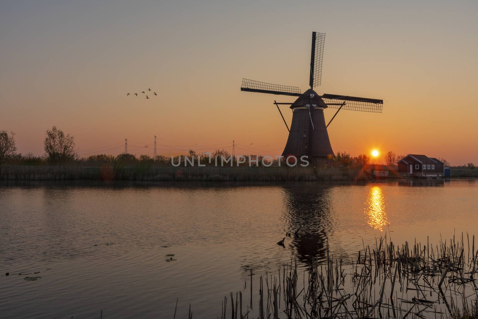 Sunrise on the alignment of windmills reflected on the calm water in the long canal 