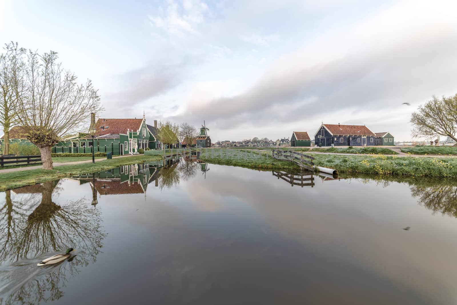 ZAANSE SCHANS, 14 April 2019 - Reflection of the wooden green houses topped with dark orange color roof reflected on the calm water of the canal