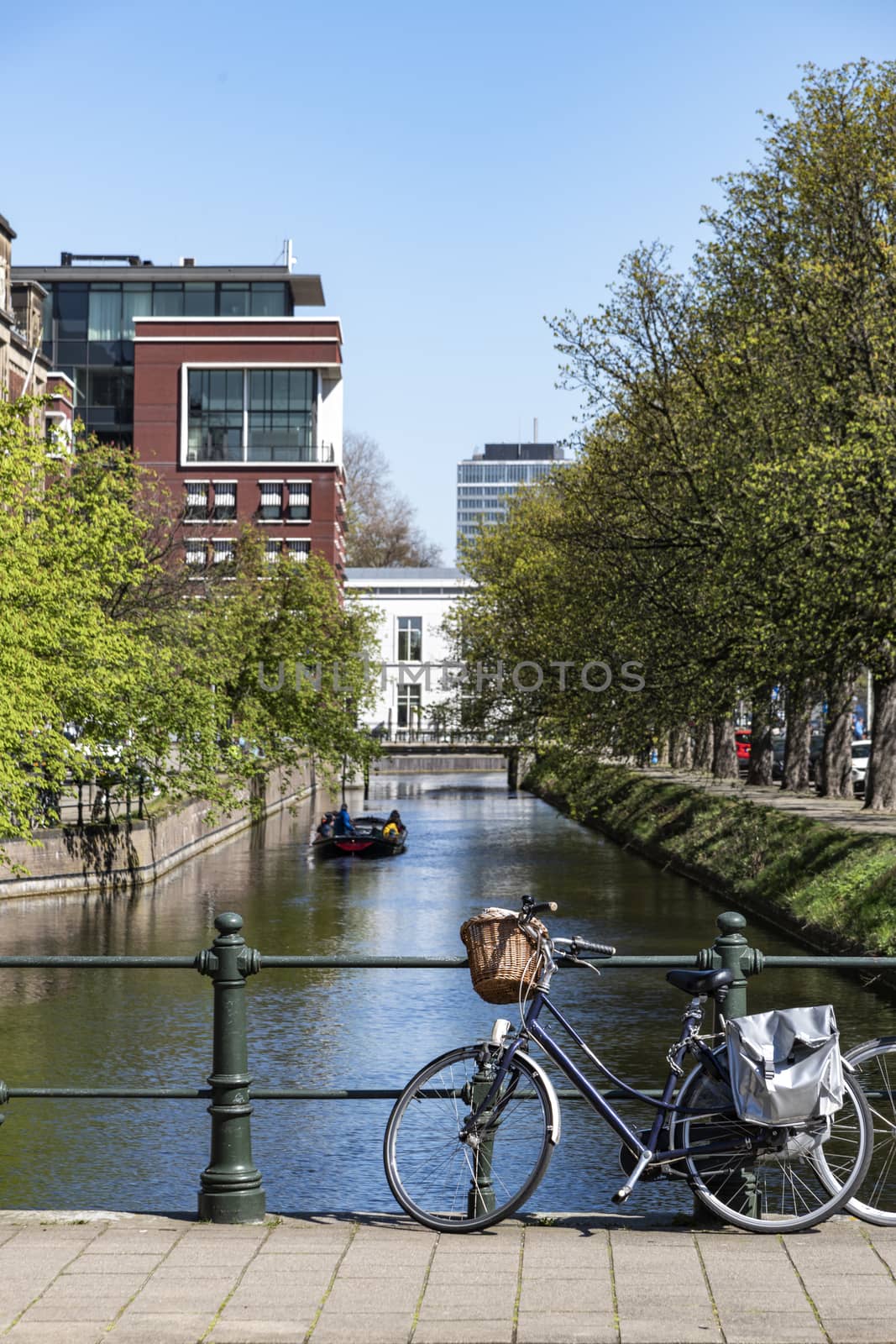 Dutch casual bicycle parking against the fence of a small bridge and road over calm canal through The Hague city under a cloudless sky, Netherlands by ankorlight
