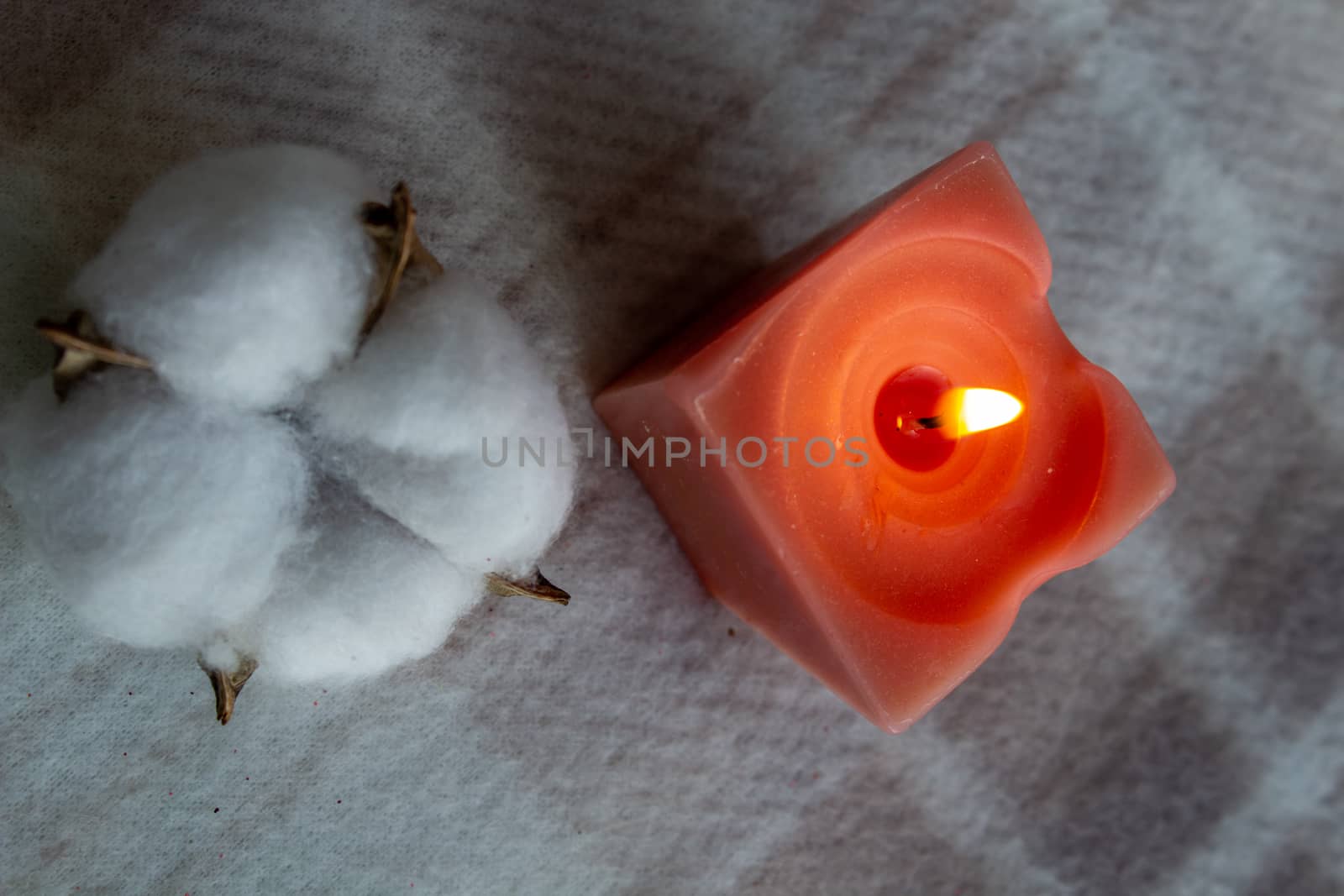 decoration, hygge and cosiness concept - burning wite fragrance candle and cotton flower on knitted blanket