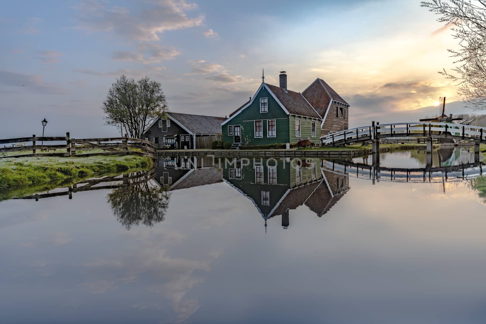 Long exposure of a reflection of the wooden green houses topped with dark orange color roof reflected on the calm water of the canal