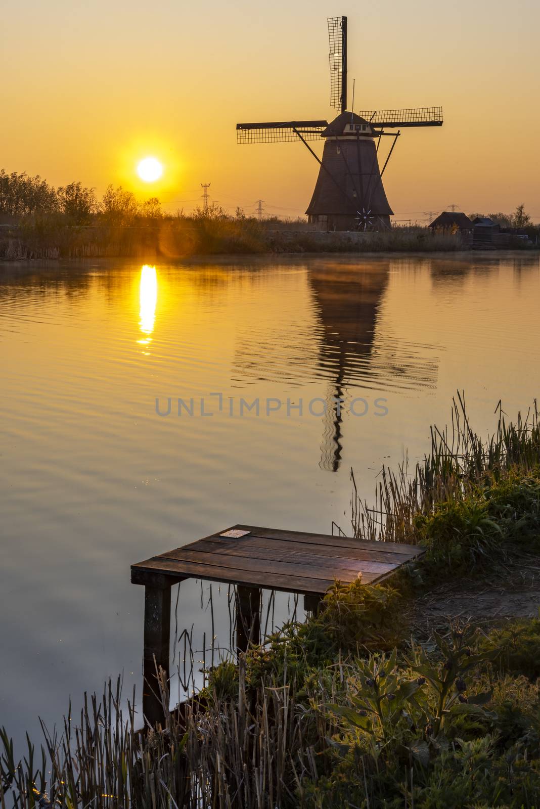 Embarquement at the edge with the calm water in the long canal during facing a windmill reflection in the burning sunrise color morning