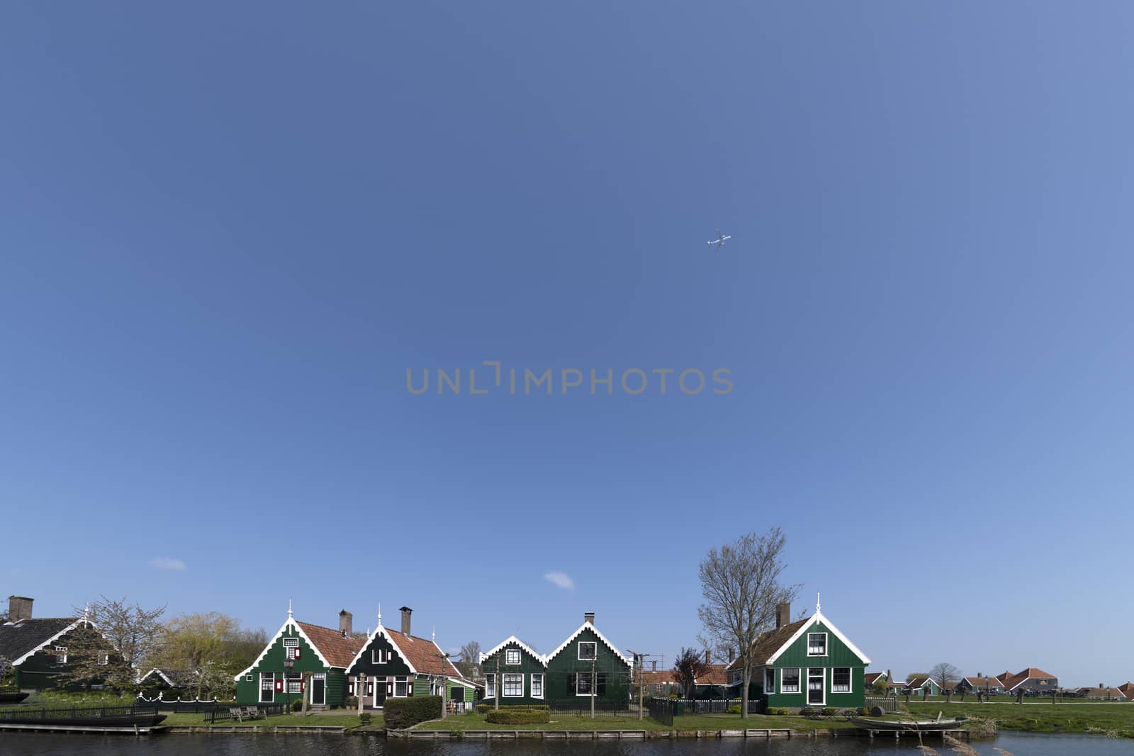 Plane flying above the Dutch green rural houses at the edge of the canals in the clear blue sunny sky