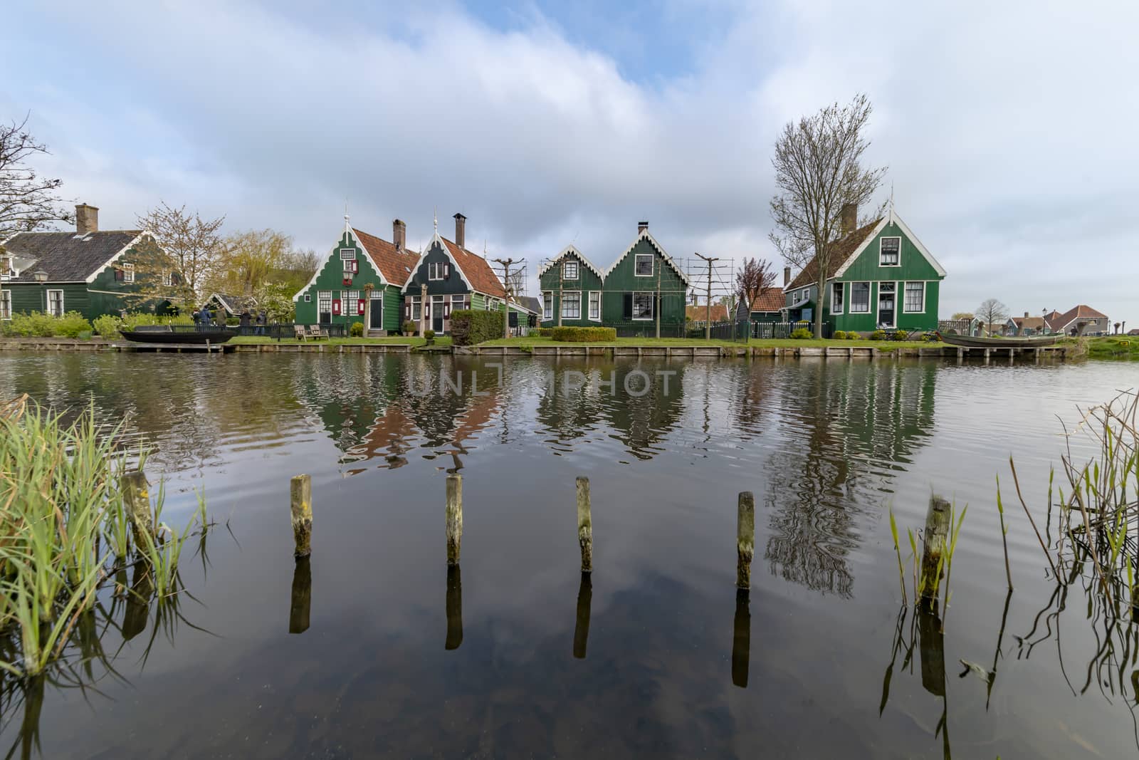 View of a reflection of the wooden green houses topped with dark orange color roof reflected on the calm water of the canal from the opposite side of the canal