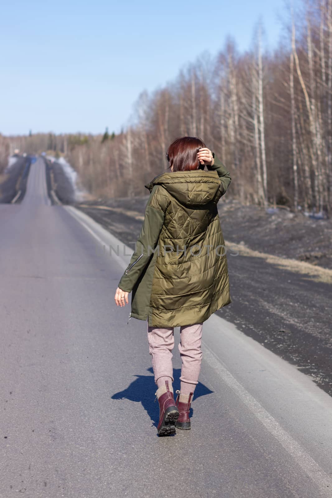 A young woman walks by the side of the road. Road in the forest by AnatoliiFoto