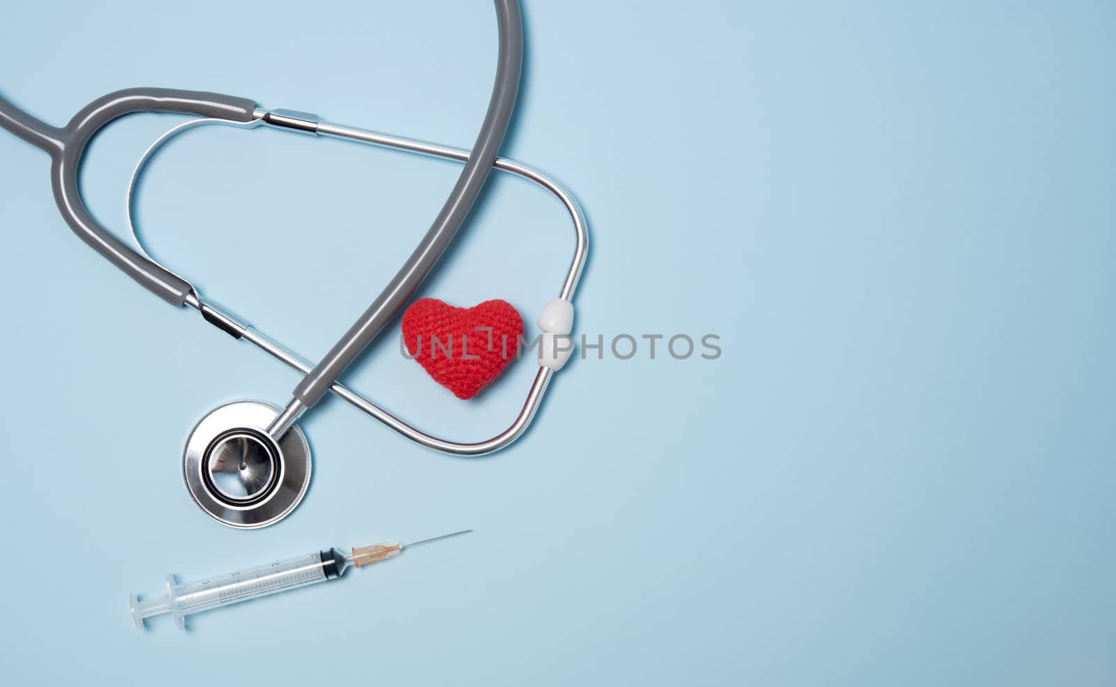 medical equipment stethoscope with red heart and syringe on blue copy space background.