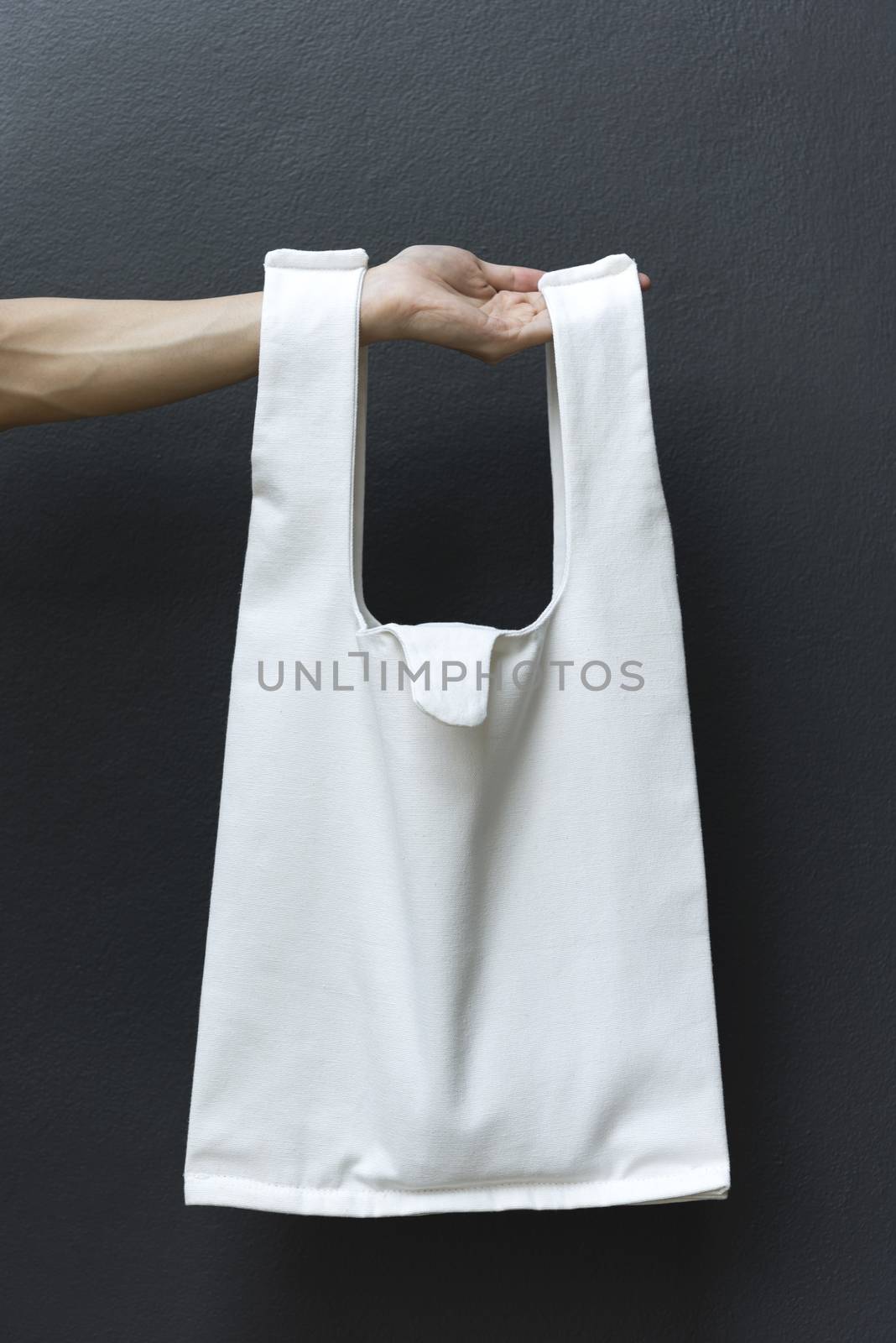 Hand Holding bag canvas fabric for mockup blank template on black wall background.