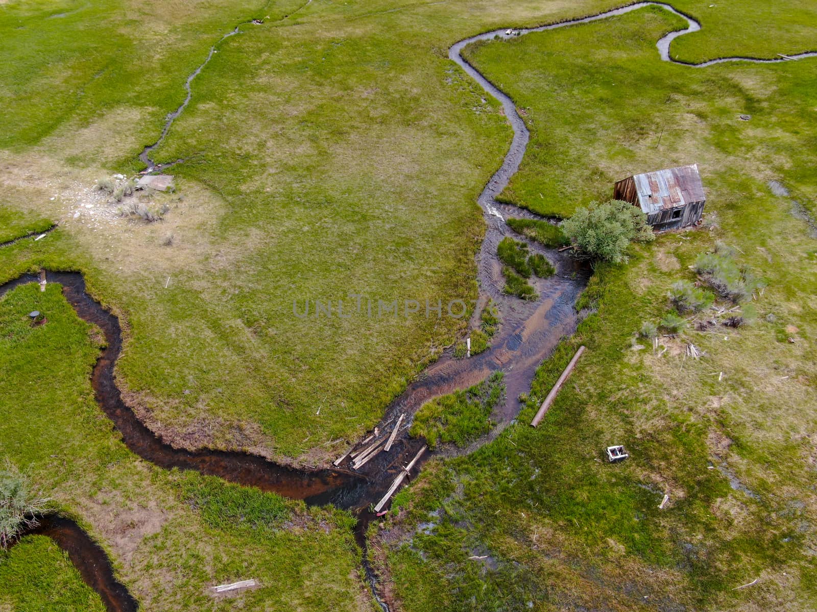 Aerial view of abandoned little small wooden house barn next small river in the green valley of a mountain, Aspen Spring, Mono County, California, USA. 