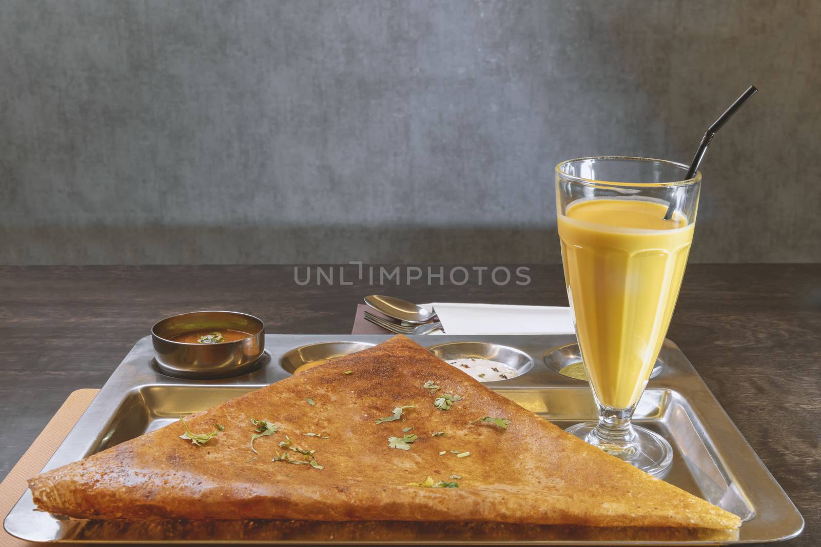Indian vegetarian pancake served with mango juice on a steal plate and several type of sauce