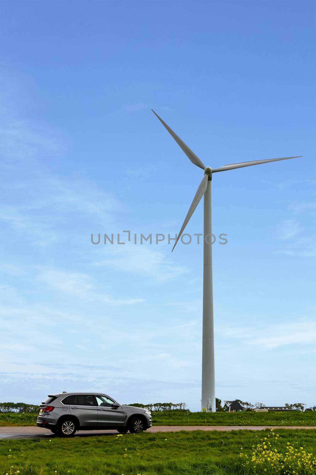 Wind turbine generating electricity under a blue sunny sky with a car parked nested to it by ankorlight