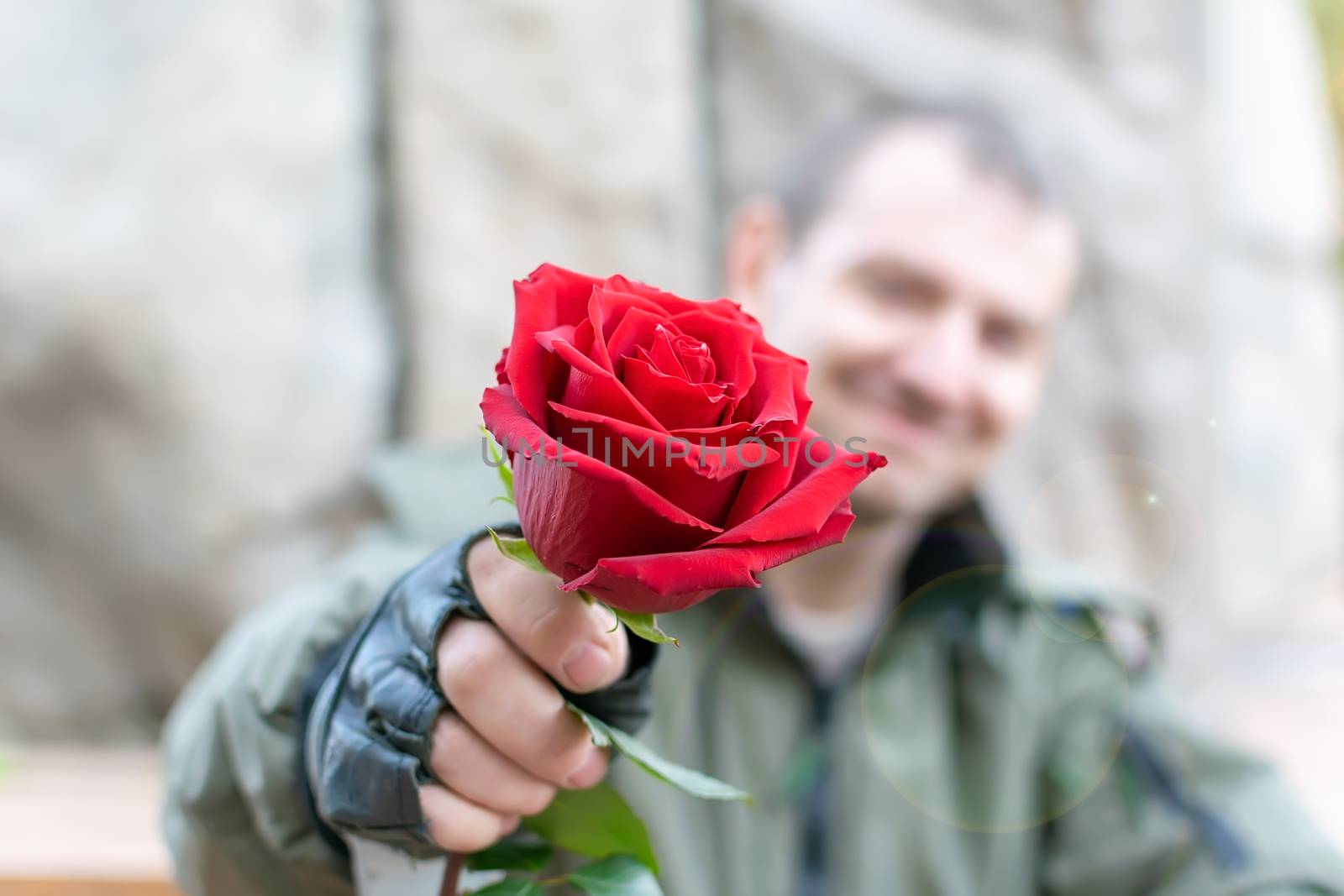 hand of a man in leather gloves and handcuffs gives a red rose flower