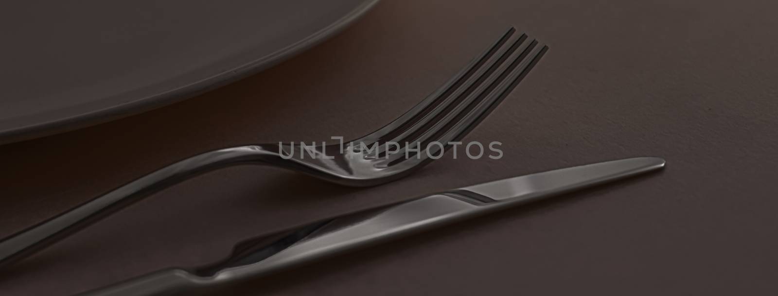 Empty plate and cutlery as mockup set on dark brown background, top tableware for chef table decor and menu branding by Anneleven