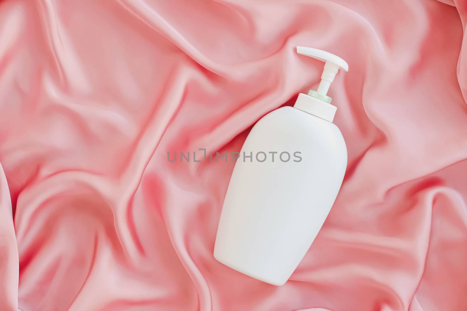 Blank label cosmetic container bottle as product mockup on pink silk background by Anneleven