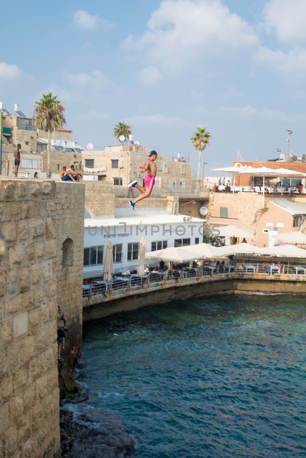 ACRE, ISRAEL - AUGUST 03, 2016: Young man jumps to the sea from the top of the ancient walls of Acre, Israel. Acre is one of the oldest continuously inhabited sites in the world
