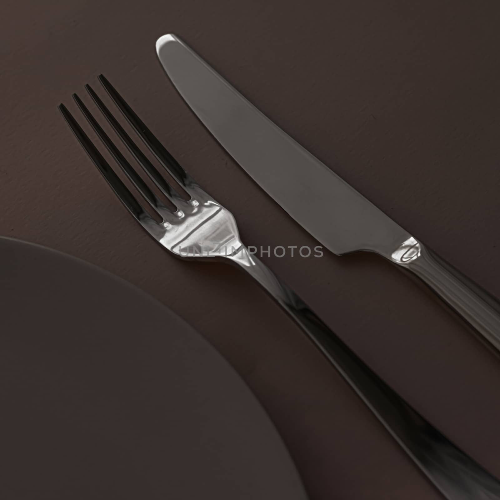 Empty plate and cutlery as mockup set on dark brown background, top tableware for chef table decor and menu branding by Anneleven