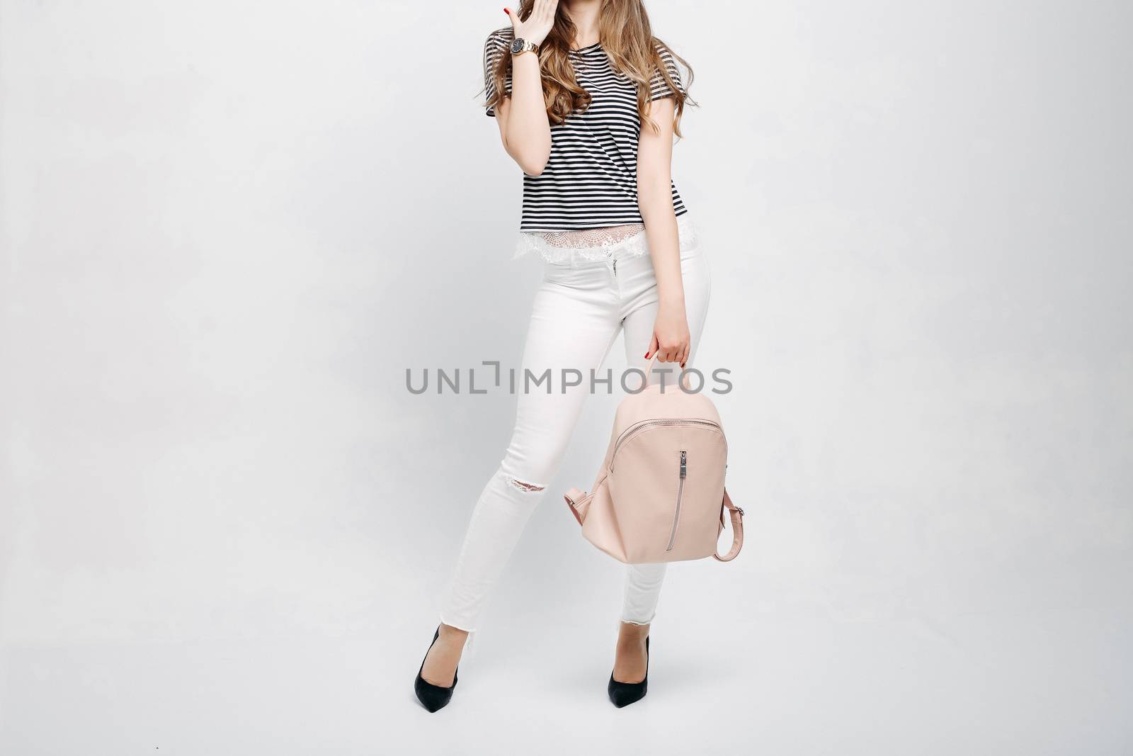 Fashionable and stylish woman with long wavy hair,red lips making duck face, surprised looking up. Girl wearing in blouse, white jeans, with leather bag, dreaming and touching face by finger. Fashion and advertising concept.