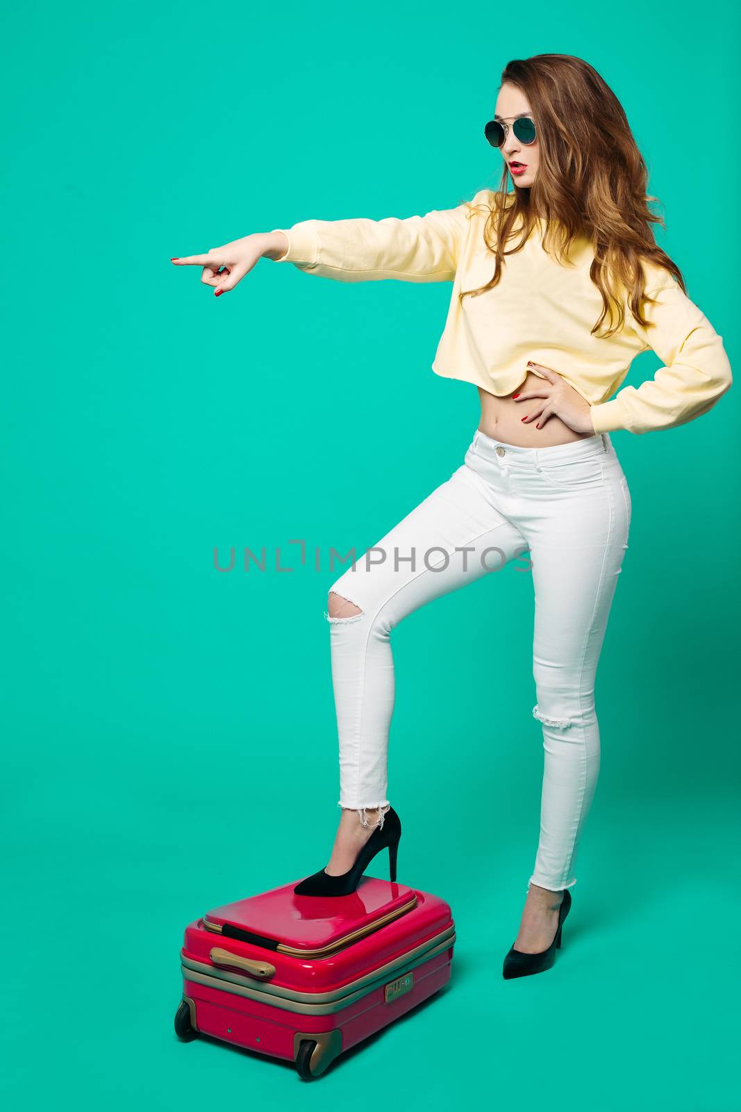 Fashionable woman in sunglasses standing on pink travel bag. by StudioLucky