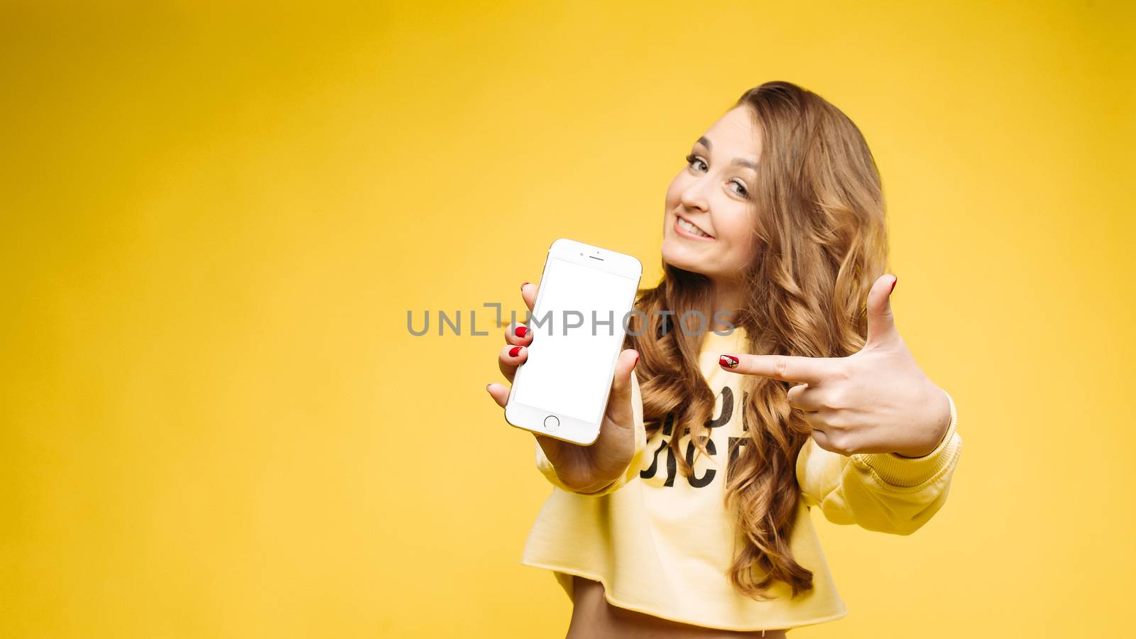 Fashionable girl holding smart phone in hand and showing at camera. by StudioLucky