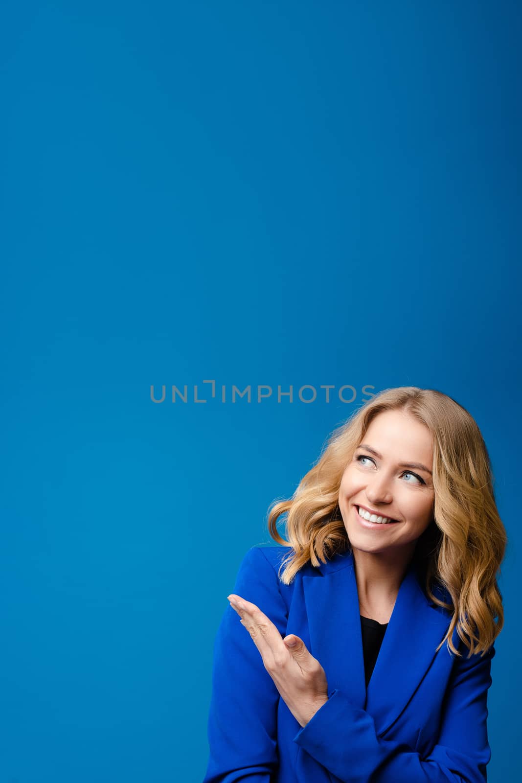 Beautiful caucasian woman with light wavy hair in a blue jacket likes it isolated on blue background