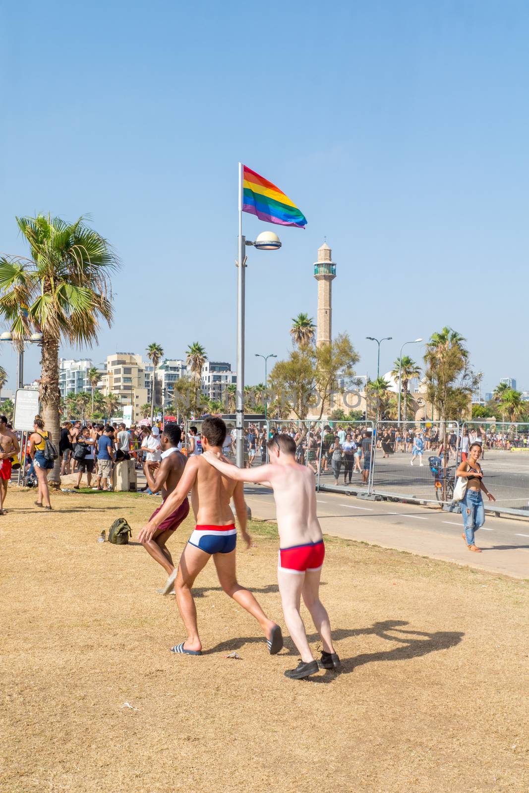 TEL-AVIV, ISRAEL - JUNE 08, 2018: Various people celebrate, the minaret of Hassan Bek Mosque and a rainbow flag, part of the annual pride parade of the LGBT community, in Tel-Aviv, Israel