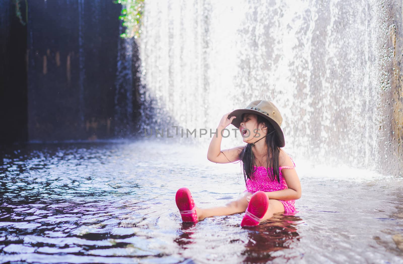 happy little asian girl wear hat playing waterfall on holiday by domonite