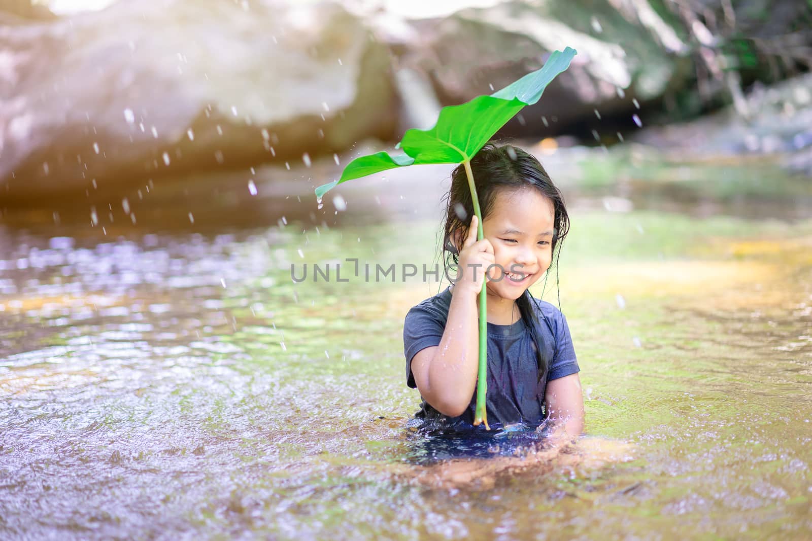 Little asian girl sitting and playing water under lotus leaf in waterfall