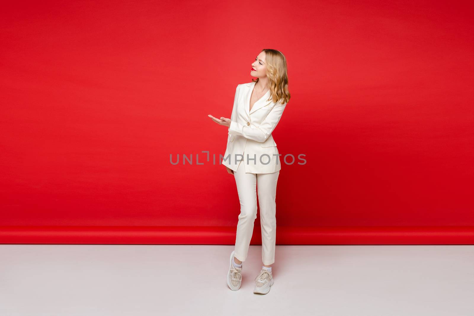 Portrait of young beautiful caucasian woman with medium blonde wavy hair and nude makeup in white suit and trainers recommends something by StudioLucky