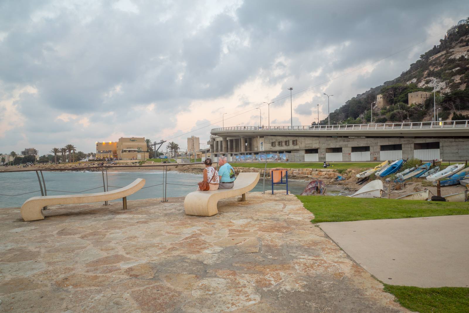 HAIFA, ISRAEL - AUGUST 06, 2018: Sunset beach scene with locals, boats, the Bat-Galim beach promenade and the Allenby Interchange, in Haifa, Israel