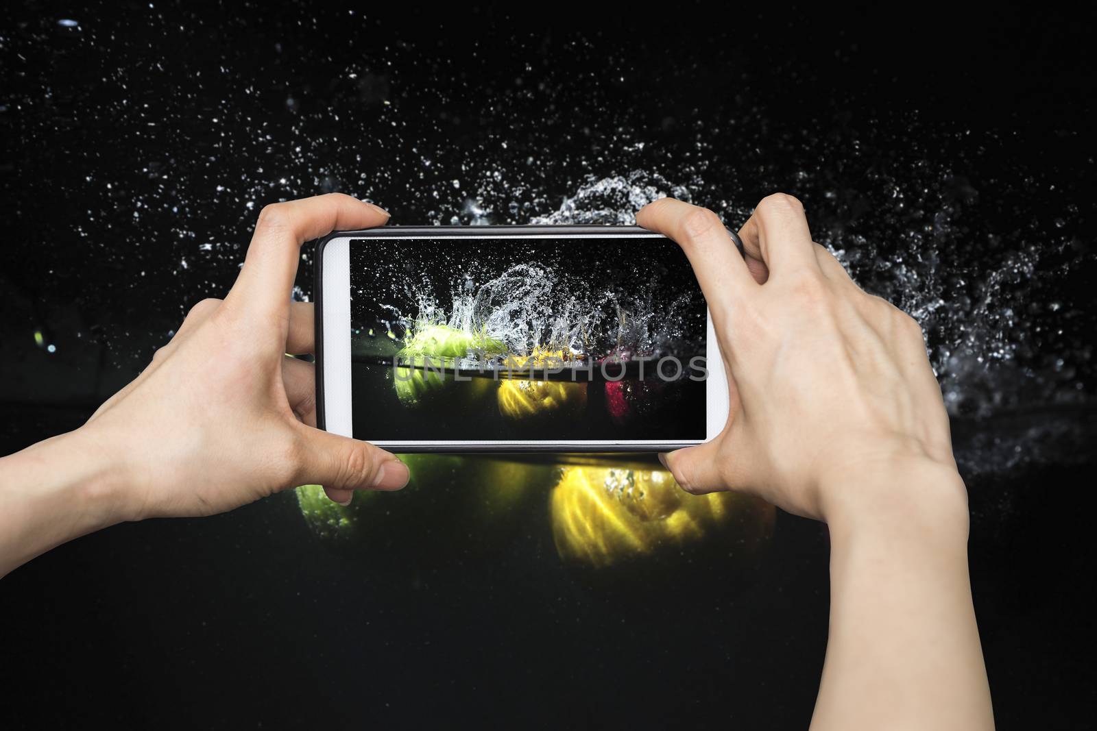 Taking pictures on mobile smart phone in Splashing fruit on water. Fresh Fruit in black background
