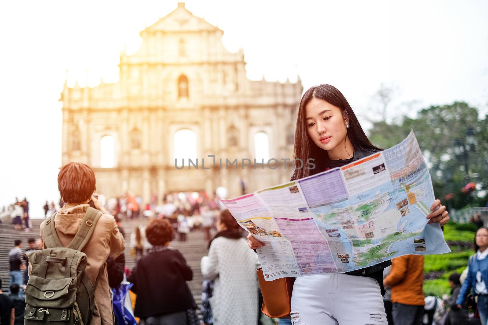 MACAU - JANUARY 11, 2016: Young female tourist with map looking for a way to View of the Ruins of St. Paul's Cathedral in Macau. It is a popular tourist attraction of Asia.