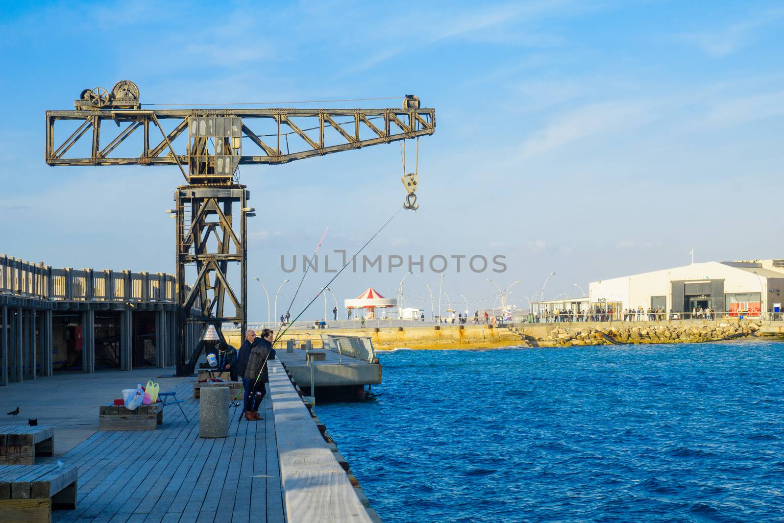 TEL-AVIV, ISRAEL - JANUARY 12, 2017: Scene with a restored crane, a commercial area, the Reading power station chimney, local fishermen and other visitors, in Tel-Aviv Port, Tel-Aviv, Israel