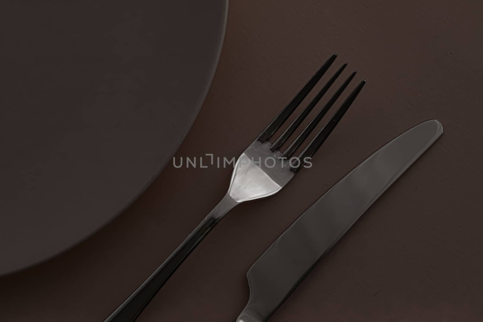 Empty plate and cutlery as mockup set on dark brown background, top tableware for chef table decor and menu branding by Anneleven