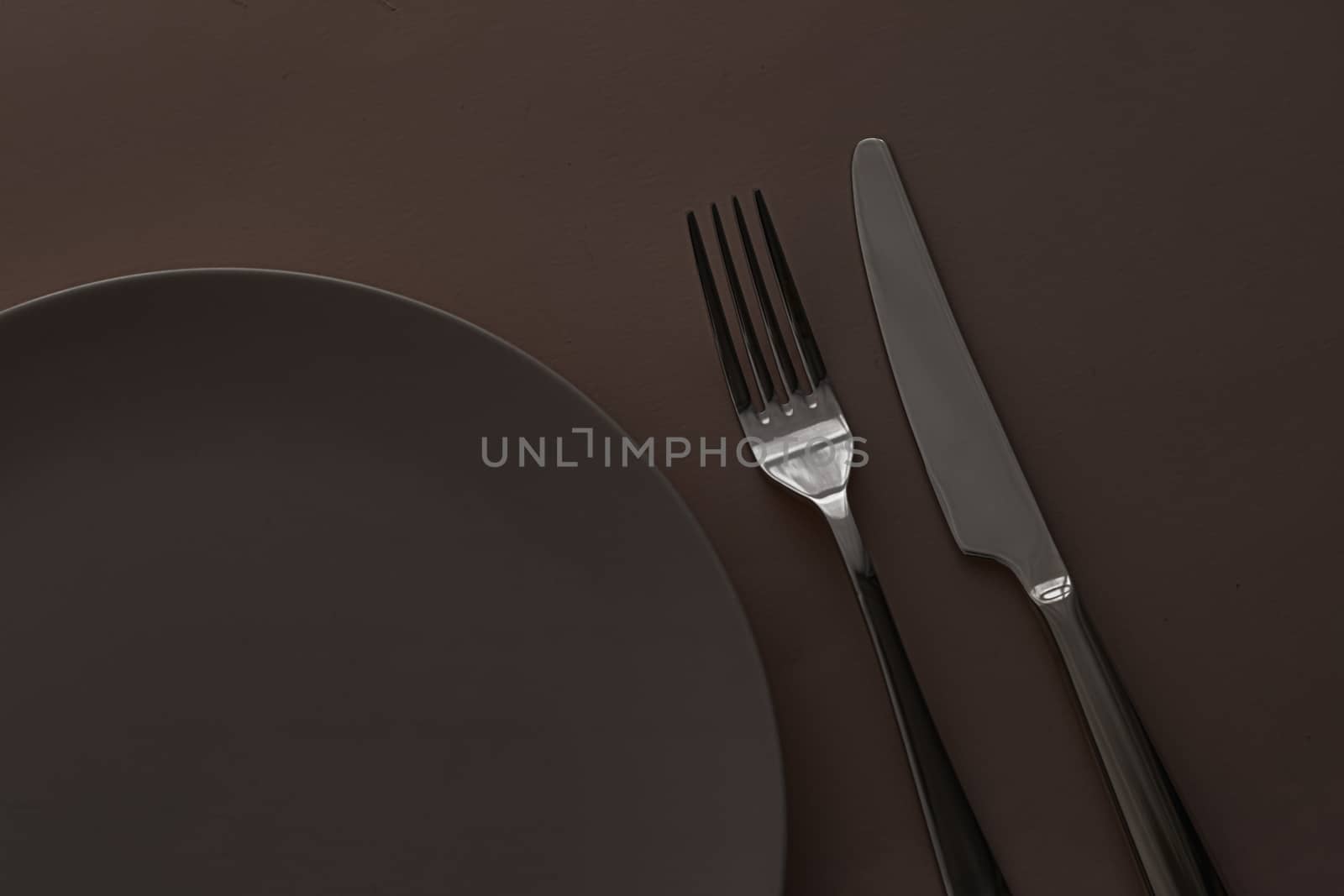 Empty plate and cutlery as mockup set on dark brown background, top tableware for chef table decor and menu branding by Anneleven