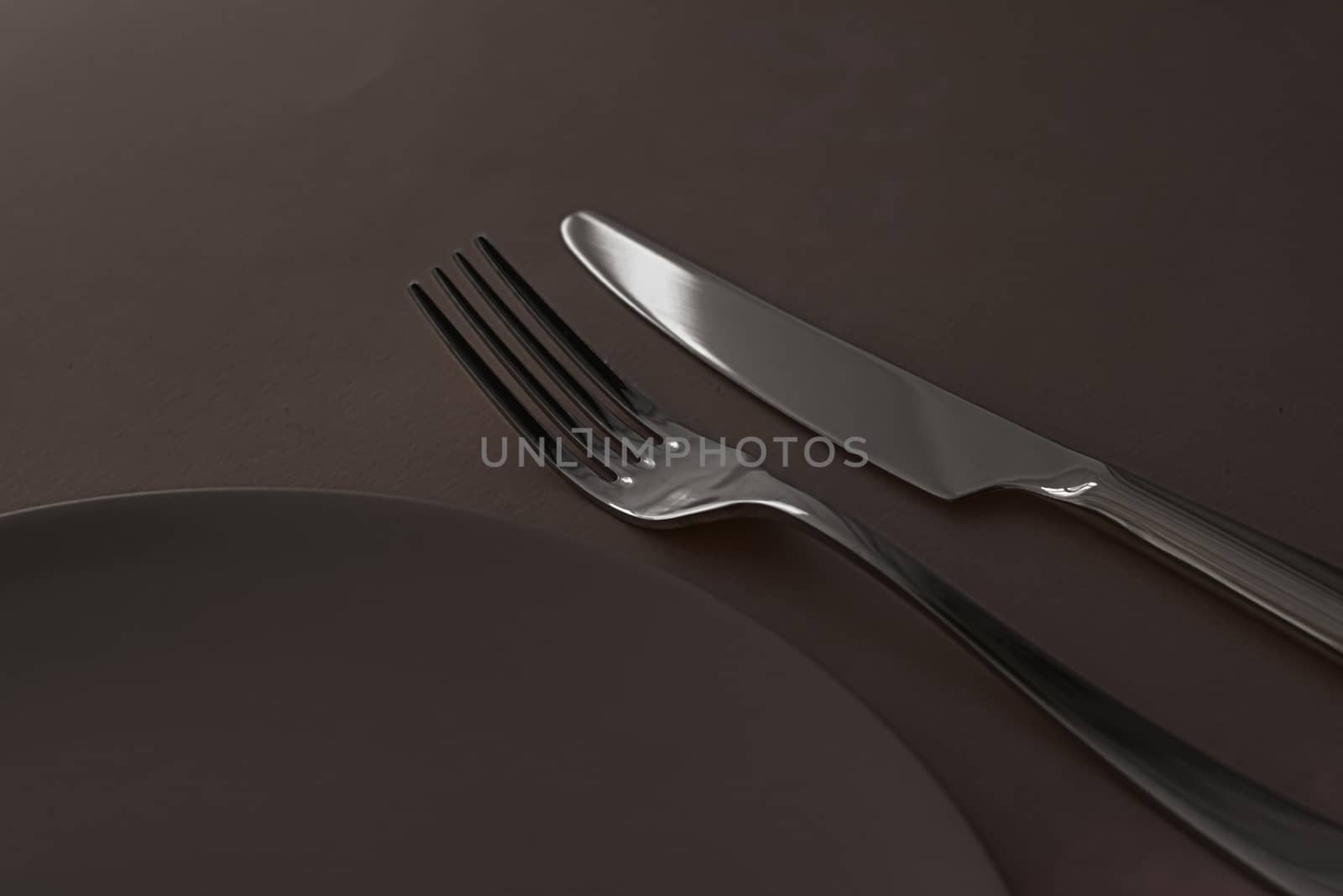 Empty plate and cutlery as mockup set on dark brown background, top tableware for chef table decor and menu branding by Anneleven