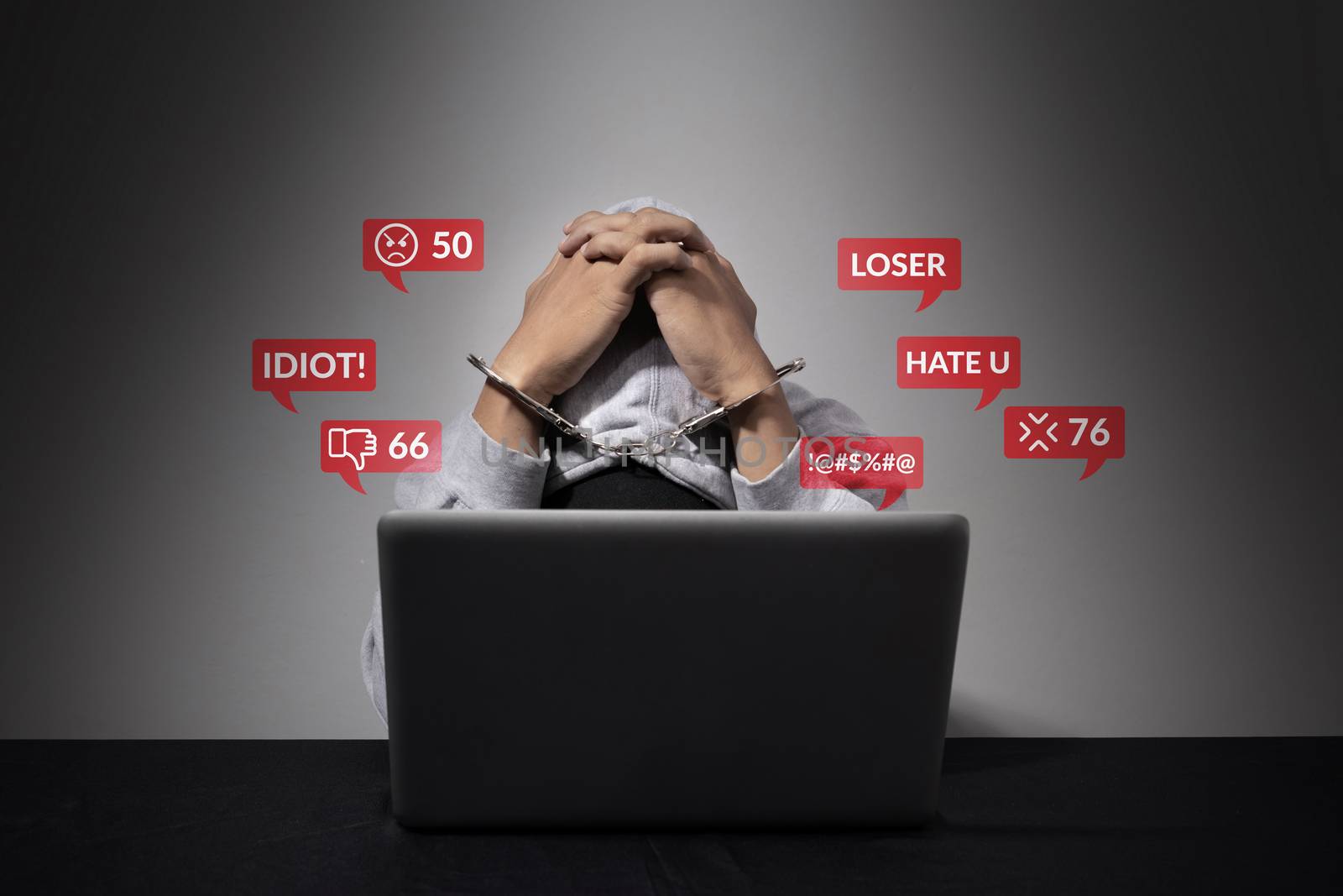 cyber bullying concept. A handcuffed man is accused of being a social defendant, bending his head in front of the laptop computer with hate speech as a cyber bullying popup message from social media. by asiandelight