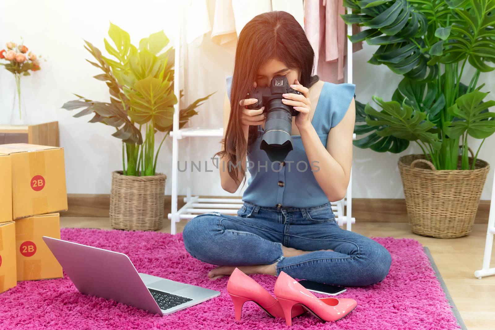 Asian woman take photo of shoe, fashion accessories for upload and selling online on website with many parcel box for shipping delivery. owner of small business working from home during self isolation