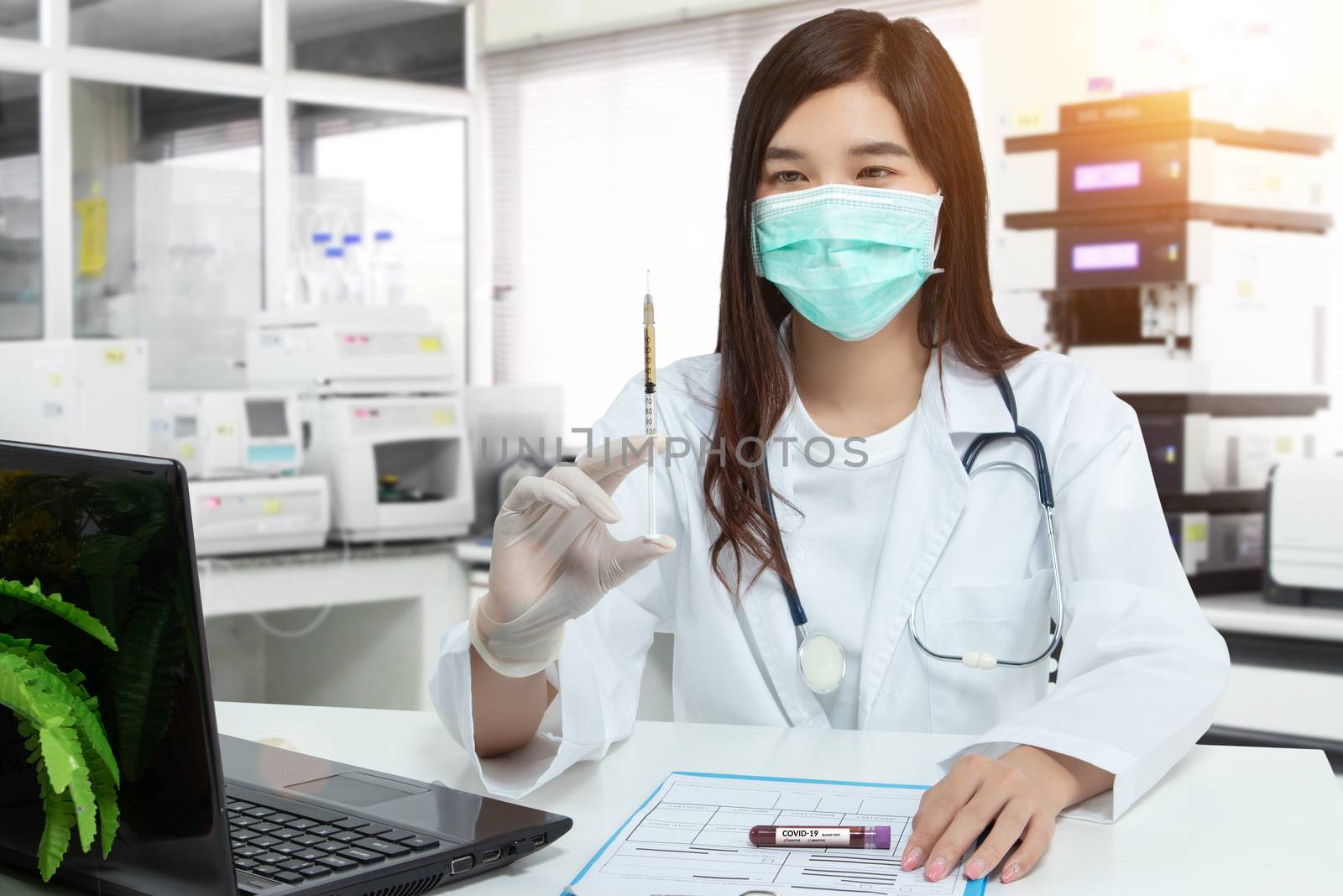 Asian doctor holds a syringe, blood sample test tube for covid-19 analyzing with patient file on desk in lab. laboratory analyzing for testing and invent drug and vaccine during Coronavirus epidemic