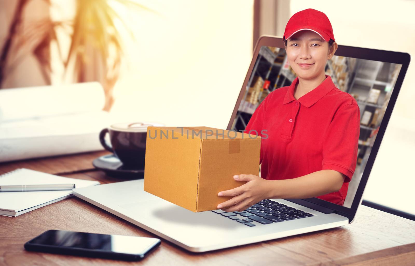 Asian delivery woman in red shirt with blur warehouse background, holding goods order in package parcel out from laptop computer. order online and delivery service concept