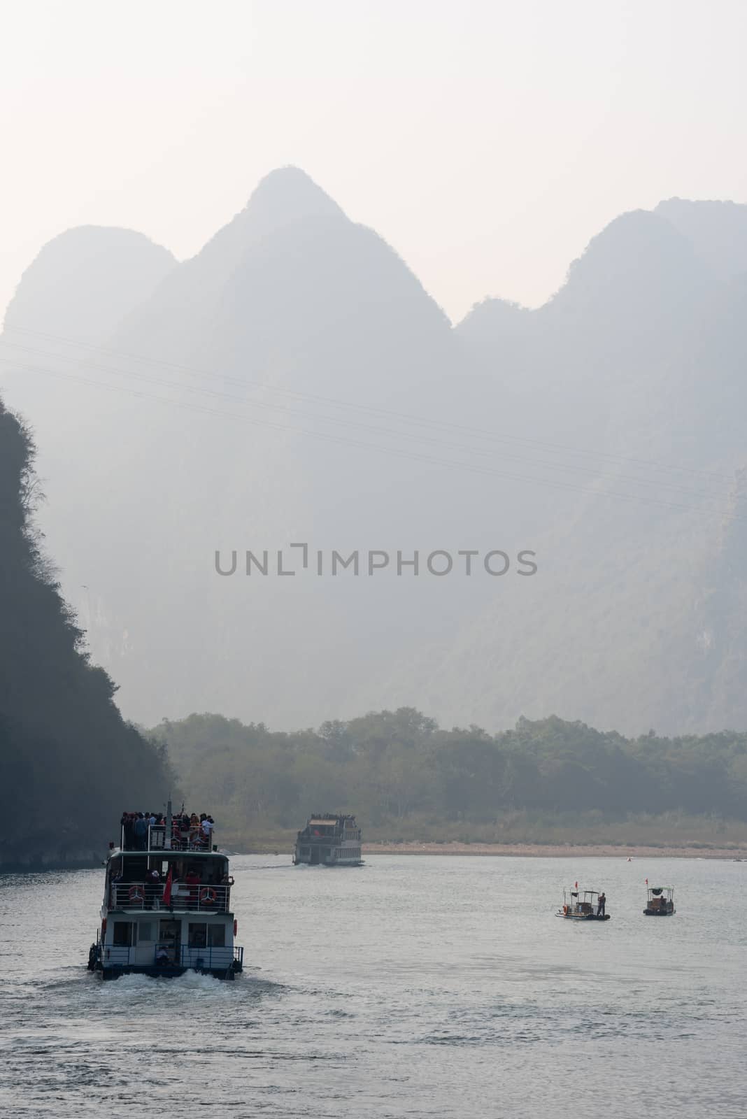 Boat on Li river cruise and karst formation mountain landscape in the fog between Guiling and Yangshuo, Guangxi province, China